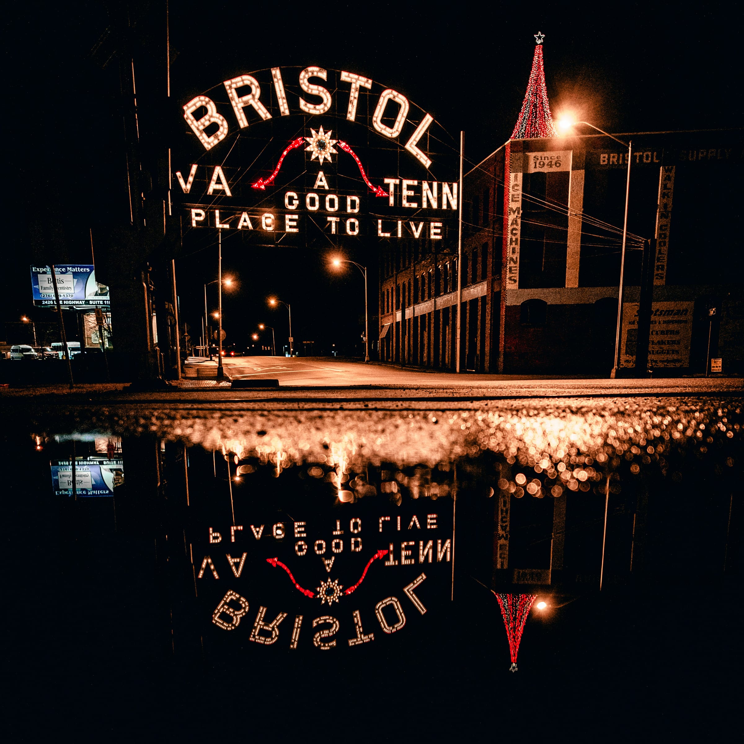 An illuminated landmark arch sign lit up at night, reflected in the wet street below.