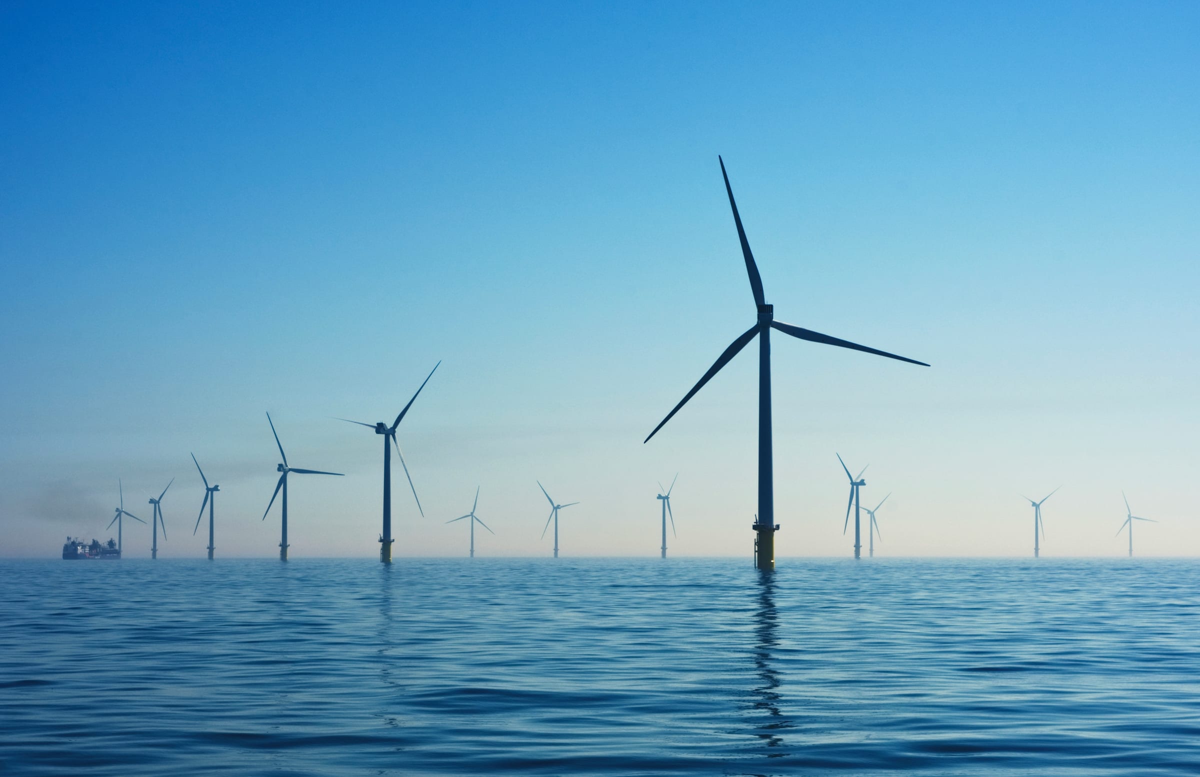 A row of offshore wind turbines standing in calm sea water under a clear sky.